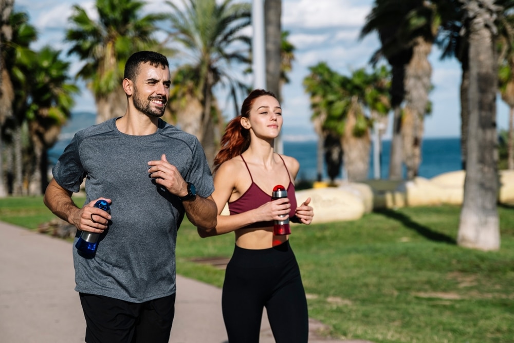 Young,Adult,Couple,Running,Together,Holding,Water,Bottles,While,Jogging.